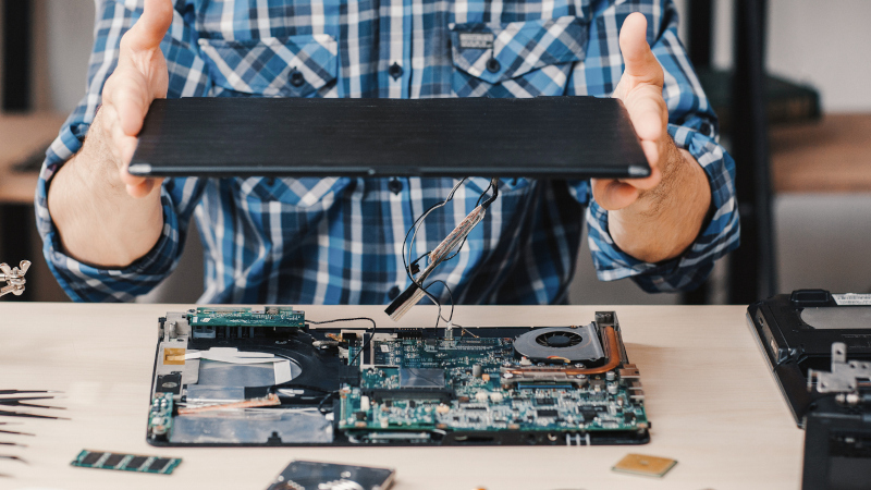 Technician studying disassembled laptop.